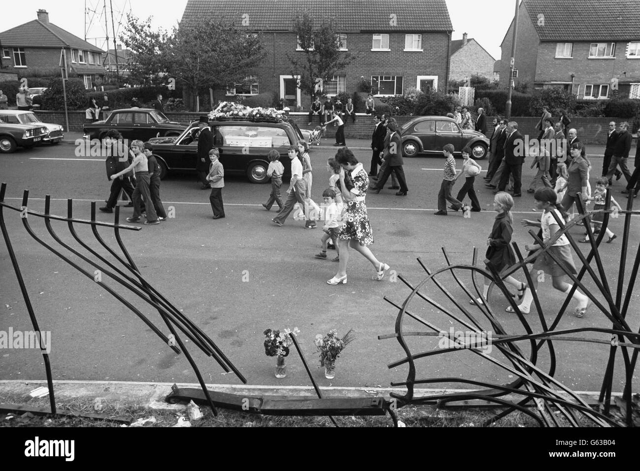 Trauernde Trauernde laufen hinter den Leichenwagen und tragen die Särge der drei jungen Maguire-Kinder, die von einem auslaufenden Auto getötet wurden, während der Trauerprozession von der römisch-katholischen Kirche in der Finnaghy Road North zum Milltown-Friedhof in Belfast. Geschäfte, Bars und Fabriken schlossen, als Arbeiter die 1,000 starke Prozession beobachteten. Menschenmengen wurden auf 5,000 Menschen geschätzt. Stockfoto