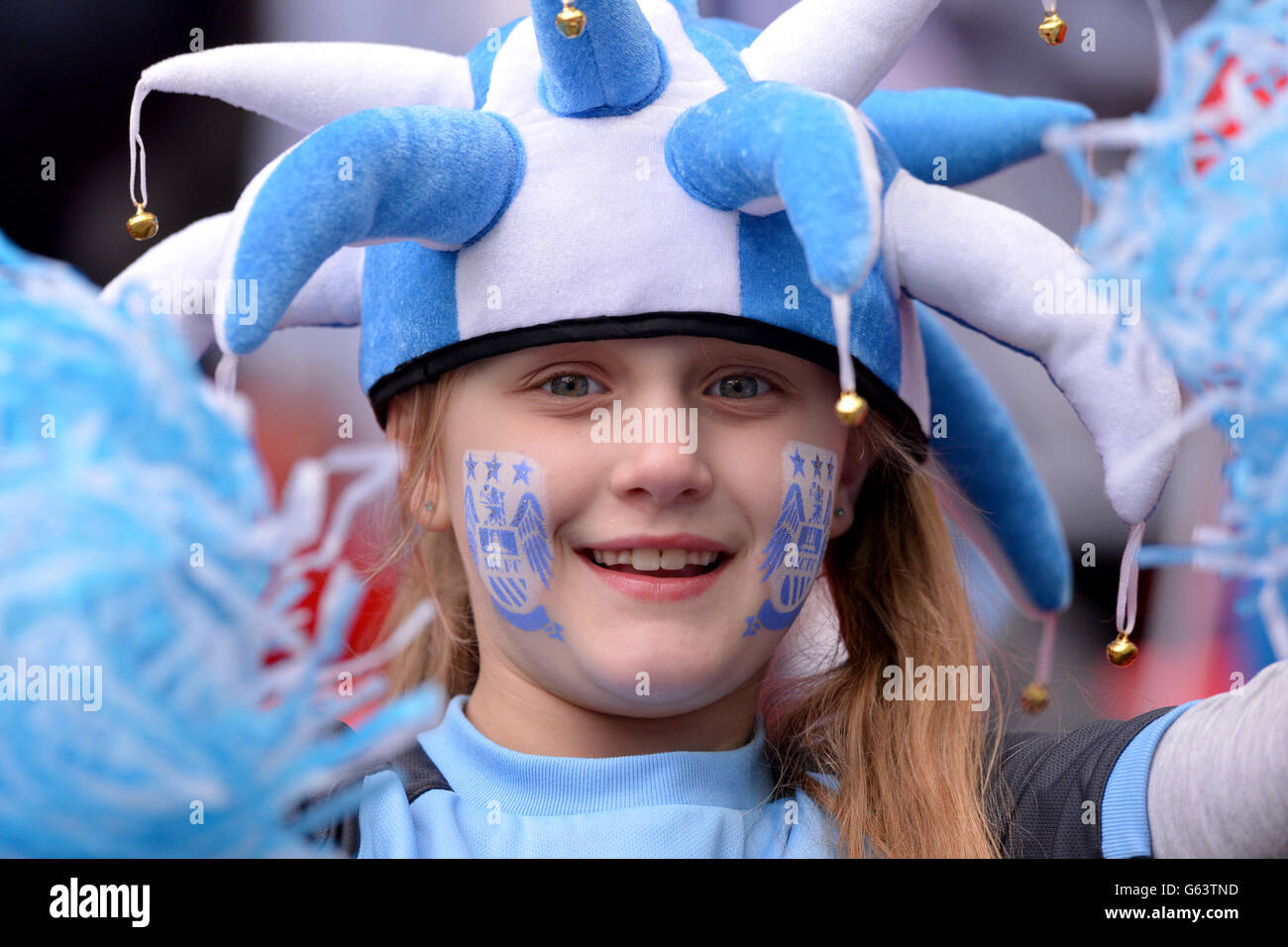 Ein junger Manchester-City-Fan mit einem Narrenhut und Gesicht malen Jubel auf ihrer Seite in den Ständen Stockfoto