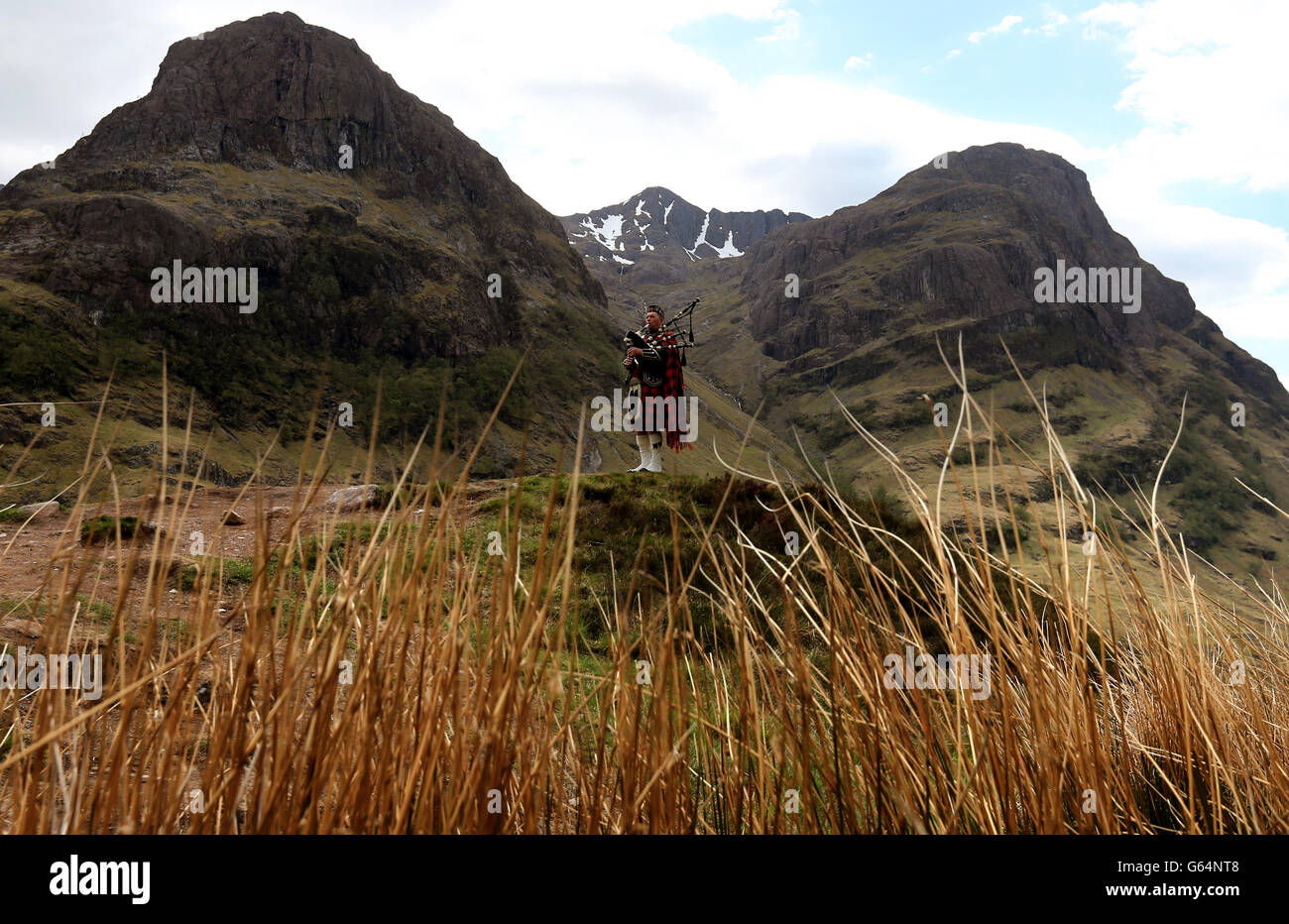 Piper Willie McPhee busting für den Tag vor der Three Sisters Bergkette in Glencoe in den Highlands. Stockfoto