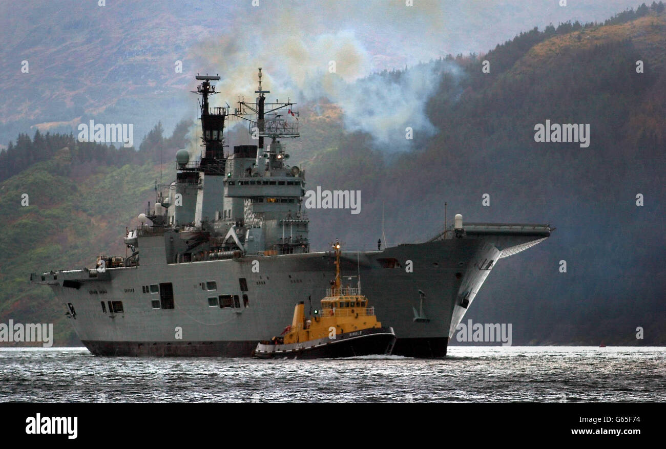 Der britische Flugzeugträger HMS Ark Royal wird von einem Schleppboot auf Loch Long begleitet, als er zum Standort Glen Douglas in Schottland auffährt. Die Arche Royal wird dort Geschäfte machen, bevor sie sich auf einen Einsatz begibt, der sie ins Mittelmeer und möglicherweise in den Golf führen wird. * 16/1/03: Das mächtigste Kriegsschiff Großbritanniens sollte von Schottland aus in See stechen, nachdem es seine letzten Vorbereitungen für einen möglichen Krieg im Golf abgeschlossen hatte. HMS Ark Royal sollte die Waffenbasis Glen Douglas am Ufer des Loch Long, Argyll, verlassen und in Richtung Mittelmeer fahren, wo sie teilnehmen wird Stockfoto