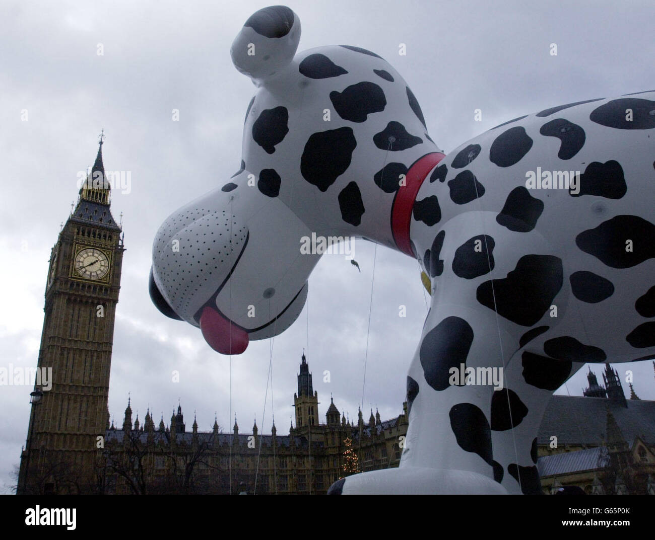 Ein riesiger aufblasbarer Hund scheint den Big Ben in London während der diesjährigen Neujahrsparade in den Schatten zu stellen. Mehr als 10,000 Darsteller erduldeten einen feuchten Start ins Jahr 2003, um die Route von außerhalb der Houses of Parliament in Westminster, im Zentrum Londons, nach Piccadilly zu gehen. * das farbenfrohe Spektakel, bei dem einheimische Acts sowie einige aus Japan und den Vereinigten Staaten zu sehen waren, stand in scharfem Kontrast zu dem Mangel an offiziellen Feierlichkeiten für das neue Jahr in London gestern Abend. Stockfoto