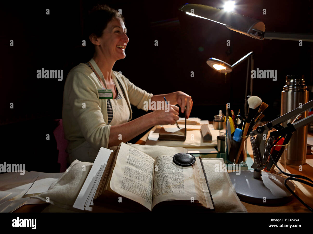 Sara Lennox-Cook, eine Papierkonservatorin, arbeitet an einer Sammlung von wasserbefleckten Büchern im Roten Raum in der Wimpole Hall des National Trust in Cambridgeshire. Stockfoto