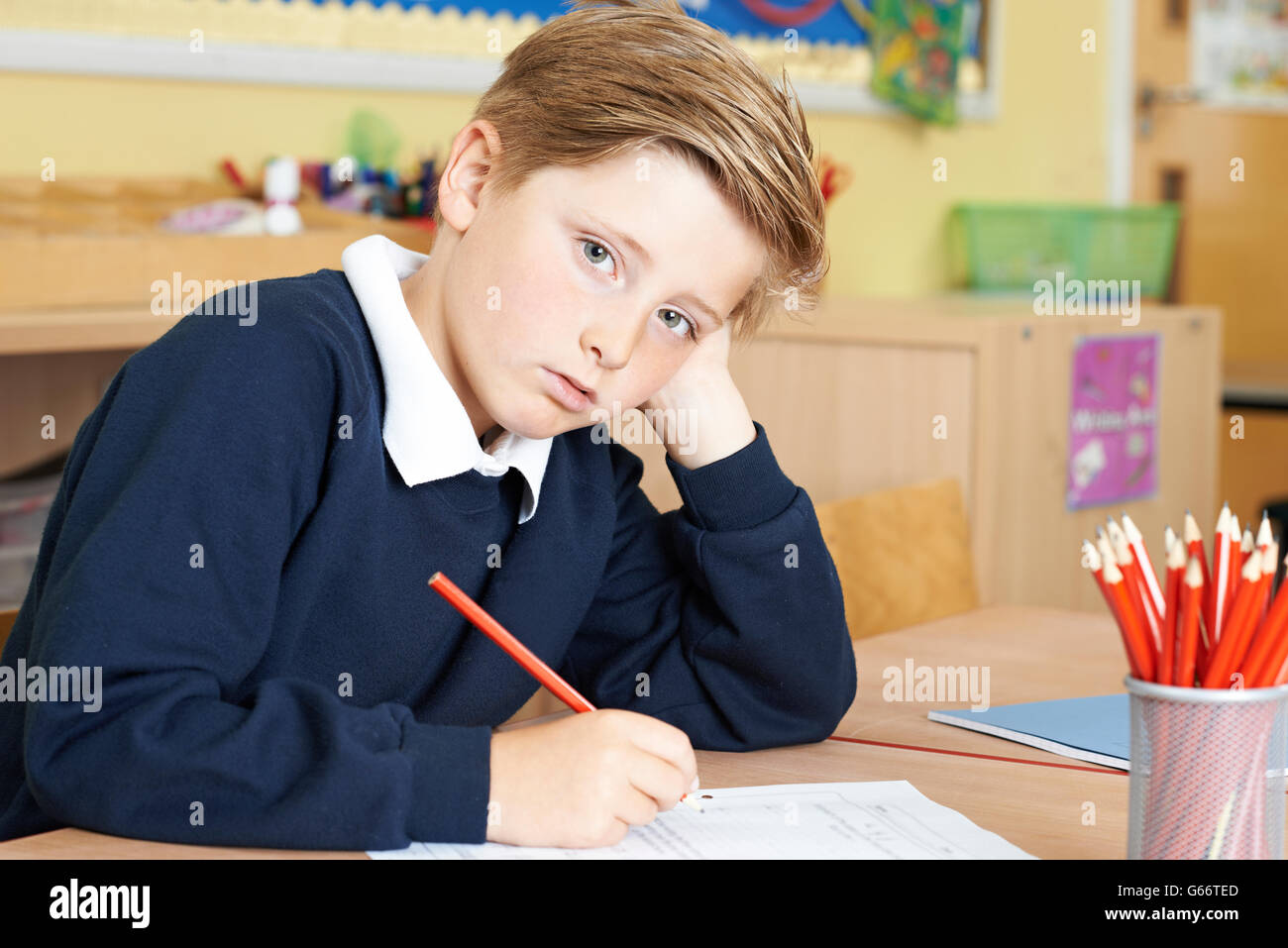 Gelangweilt männlichen Grundschule Schüler am Schreibtisch Stockfoto