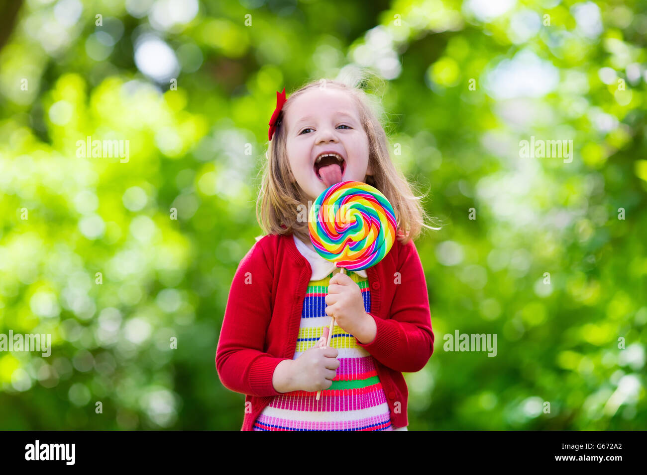 Niedliche kleine Mädchen mit großen bunten Lollipop. Kind, essen Süßigkeiten Bar. Süßigkeiten für kleine Kinder Stockfoto
