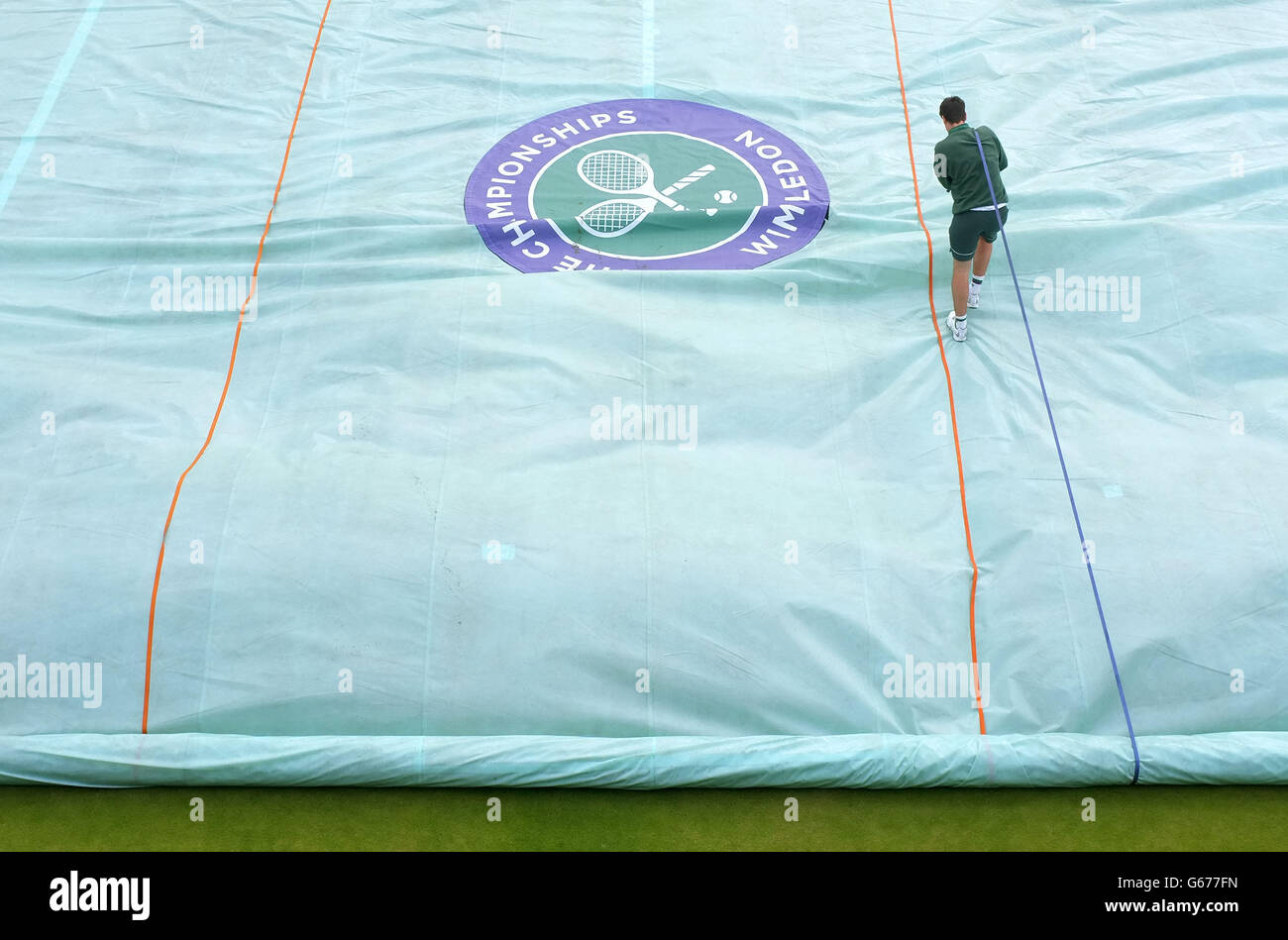 Ein Platzwart arbeitet zu Beginn des fünften Tages der Wimbledon Championships im All England Lawn Tennis and Croquet Club, Wimbledon, daran, die Abdeckung des Platzes zu entfernen. Stockfoto