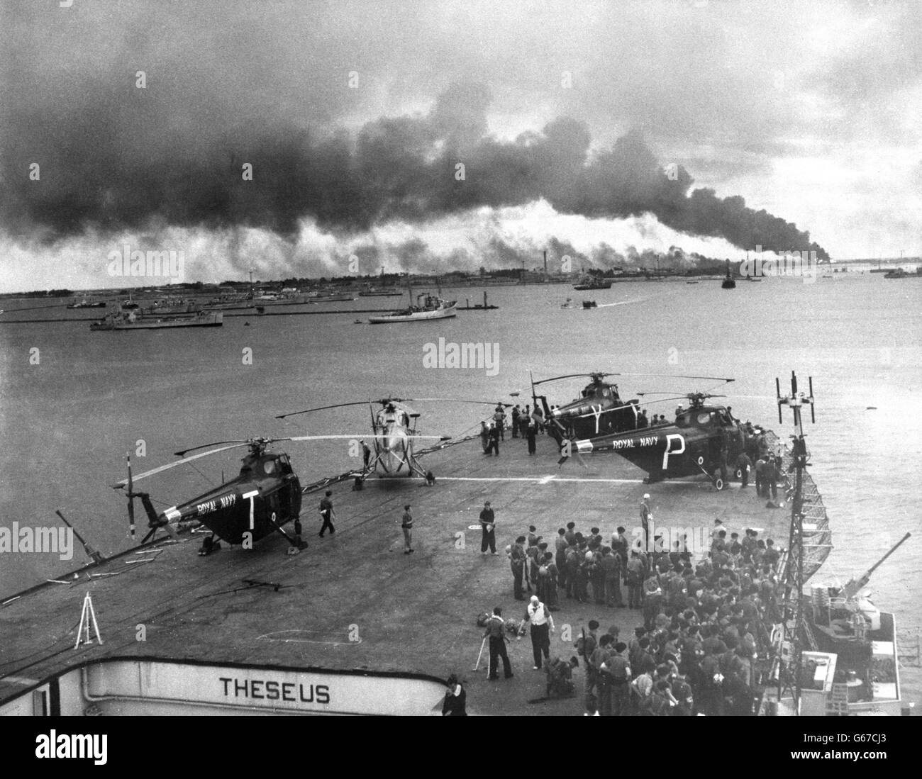 Truppen und Helikopter an Deck eines der ersten Schiffe der Royal Navy, die nach der Eroberung von Port Said, Ägypten, eindrangen, das von Rauch und Feuer umhüllt ist. Stockfoto