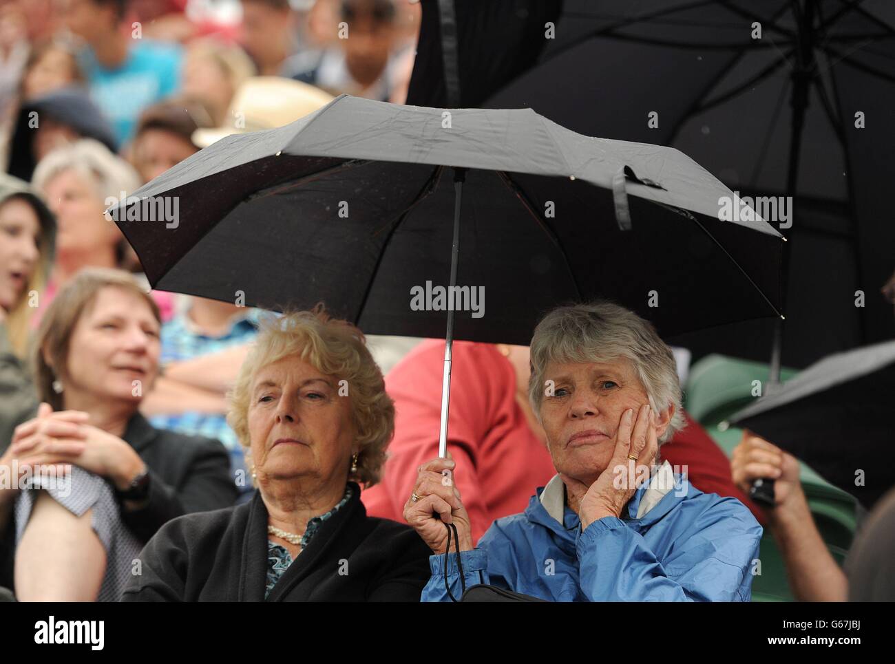 Am vierten Tag der Wimbledon Championships im All England Lawn Tennis und Croquet Club in Wimbledon schützen Fans sich mit einem Regenschirm vor dem leichten Regen. Stockfoto