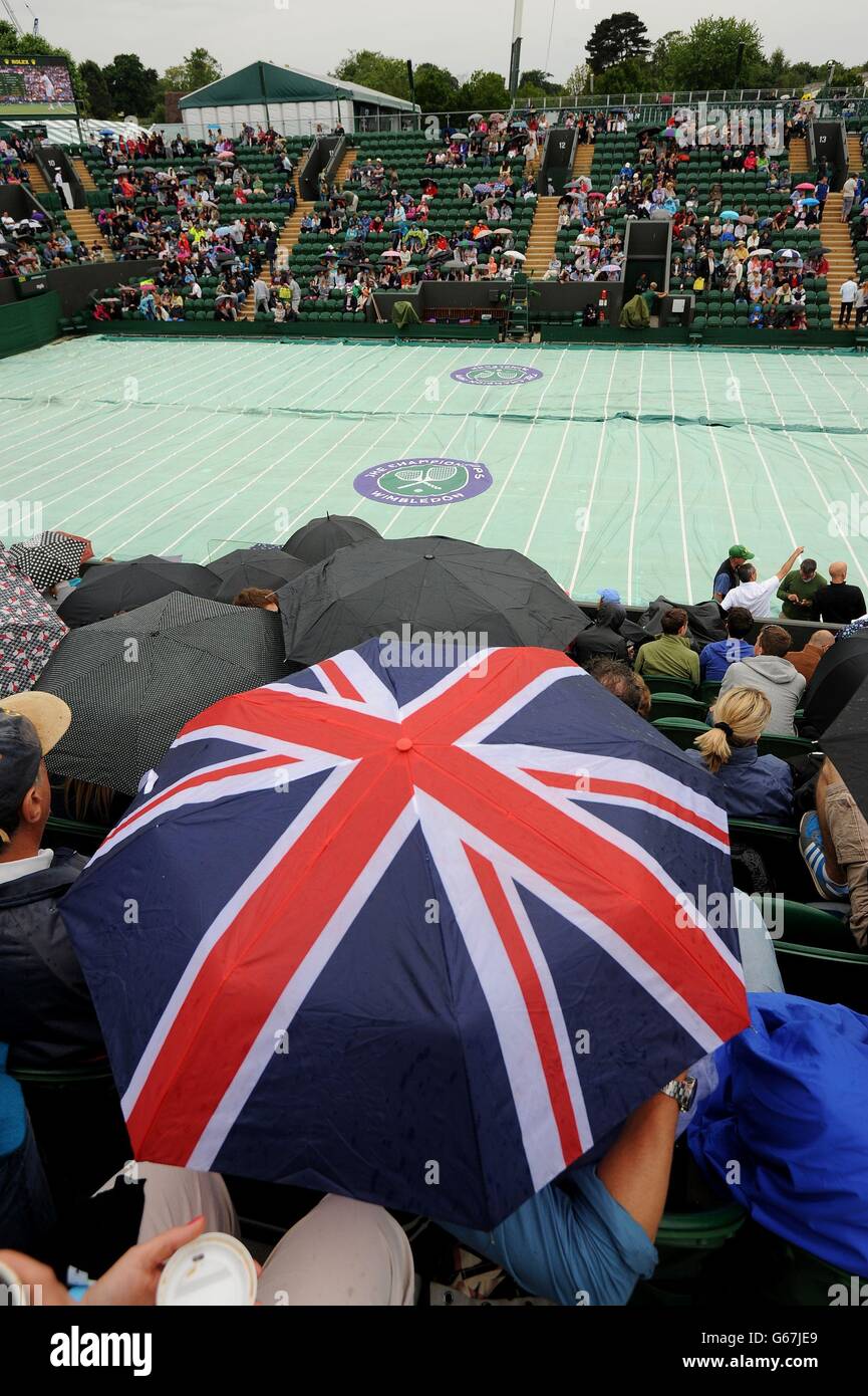 Am vierten Tag der Wimbledon Championships am All England Lawn Tennis und Croquet Club in Wimbledon schützen sich Fans vor dem Regen auf dem Platz zwei. Stockfoto