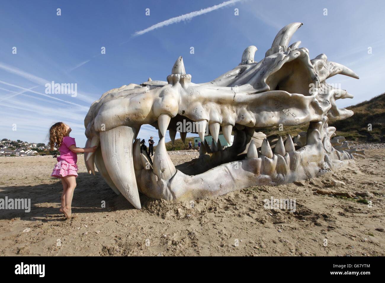 Pantha Bradbury, drei, steht vor einem 39 Meter breiten Drachen Schädel, die geschaffen wurde, um den Start von HBO Game of Thrones Saison feiern 3 auf dem Fernsehen und Film-Service, blinkbox, auf Charmouth Beach an der Jurassic Coast in Lyme Regis, Dorset. Stockfoto