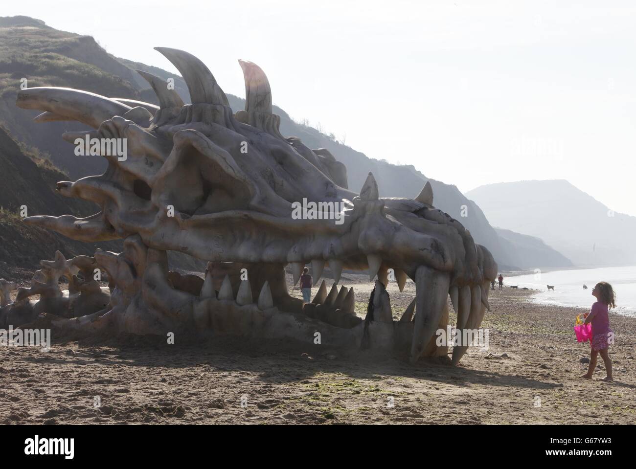 REDAKTIONELLE VERWENDUNG NUR Pantha Bradbury, drei, steht vor einem 39 Meter breiten Drachen Schädel, die geschaffen wurde, um den Start der HBOs Game of Thrones Saison feiern 3 auf dem Fernseh-und Film-Service, blinkbox, auf Charmouth Beach an der Jurassic Küste in Lyme Regis, Dorset. Stockfoto