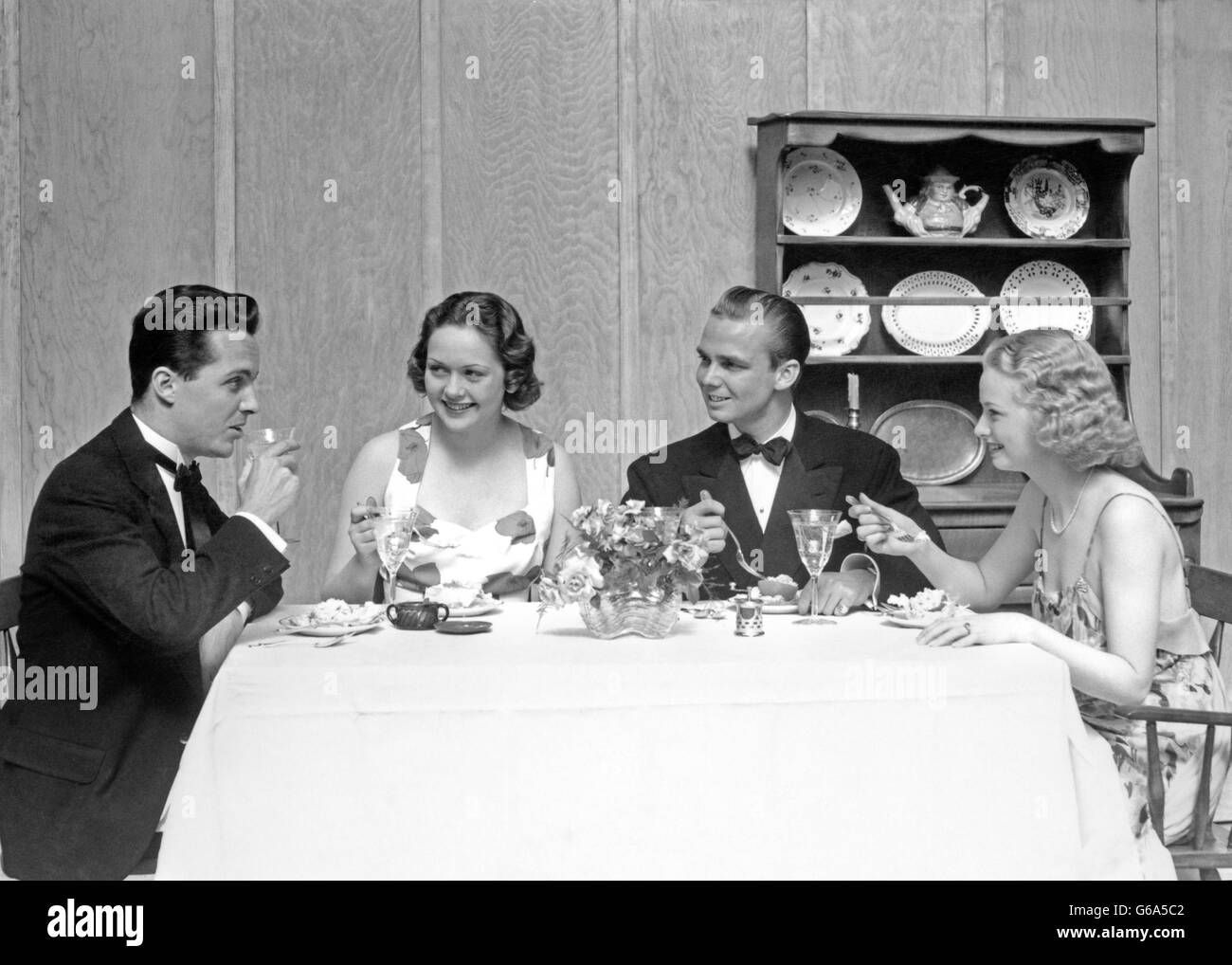 1930ER JAHREN ZWEI PAARE VIER MÄNNER UND FRAUEN SITZEN AM ESSTISCH, FORMELLE KLEIDUNG Stockfoto