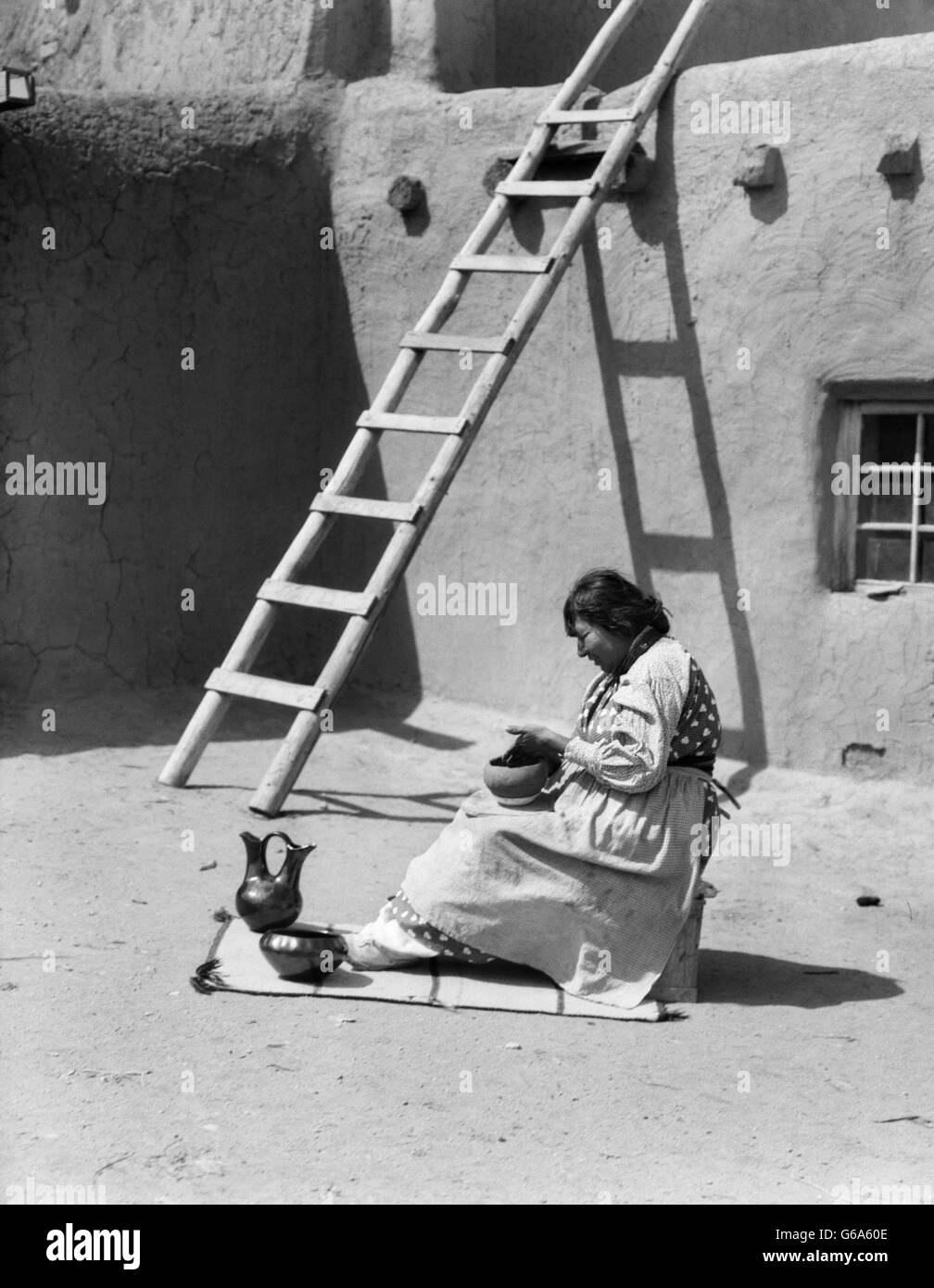 1930ER JAHREN INDIANISCHE FRAU POLIEREN KERAMIK IM FREIEN DURCH LEITER SANTA CLARA PUEBLO NEW MEXICO USA Stockfoto