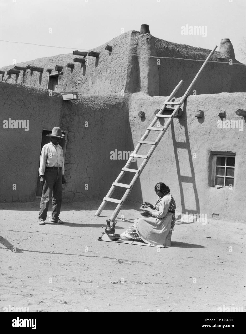 1930ER JAHREN INDIANISCHE PAAR VON ADOBE GEBÄUDE FRAU POLIEREN KERAMIK MANN BLICK AUF SANTA CLARA PUEBLO NEW MEXICO USA Stockfoto