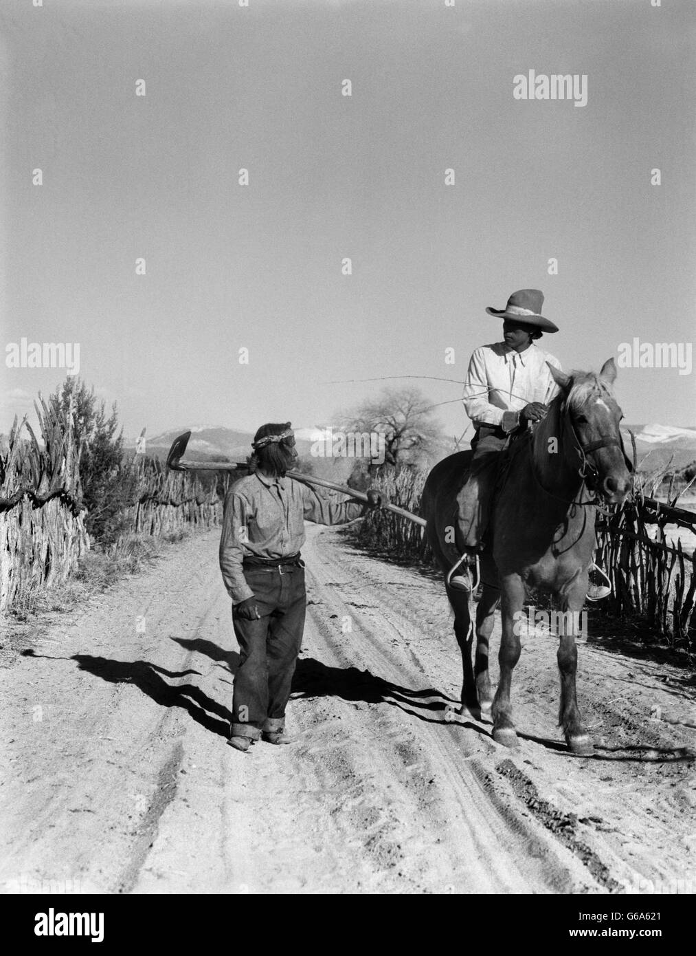 1930ER JAHREN ZWEI INDIANISCHEN MÄNNER AUF DESERT ROAD ZU FUß AUF DEM ANDEREN PFERD SPRECHEN SAN ILDEFONSO PUEBLO NEW MEXICO USA Stockfoto