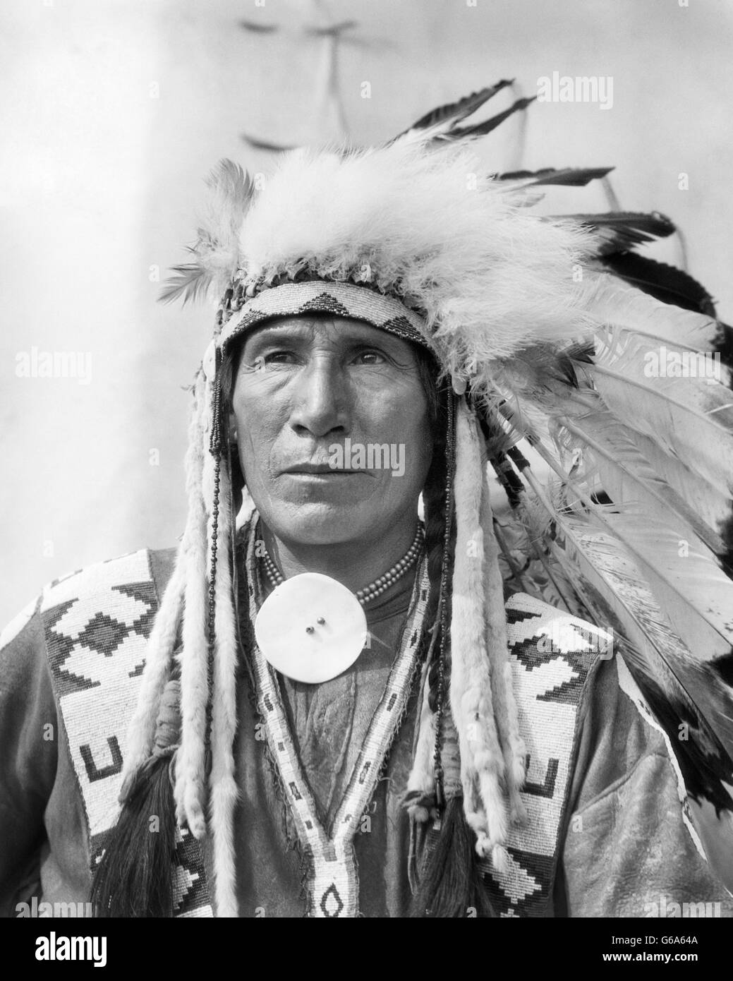 1920ER JAHRE PORTRAIT NATIVE AMERICAN INDIAN MAN CHEF SITZEN ADLER IN VOLLER KOPFSCHMUCK STONEY STAMM VON BANFF ALBERTA, KANADA Stockfoto