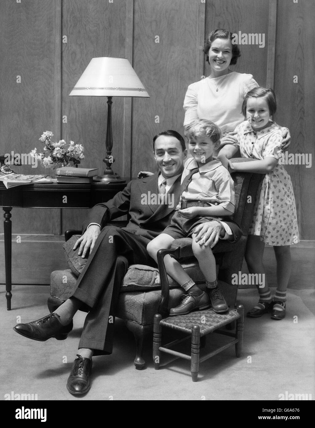1930ER JAHRE PORTRAIT LÄCHELND FAMILIE VATER MUTTER ZWEI KINDER IM WOHNZIMMER MIT BLICK IN DIE KAMERA Stockfoto