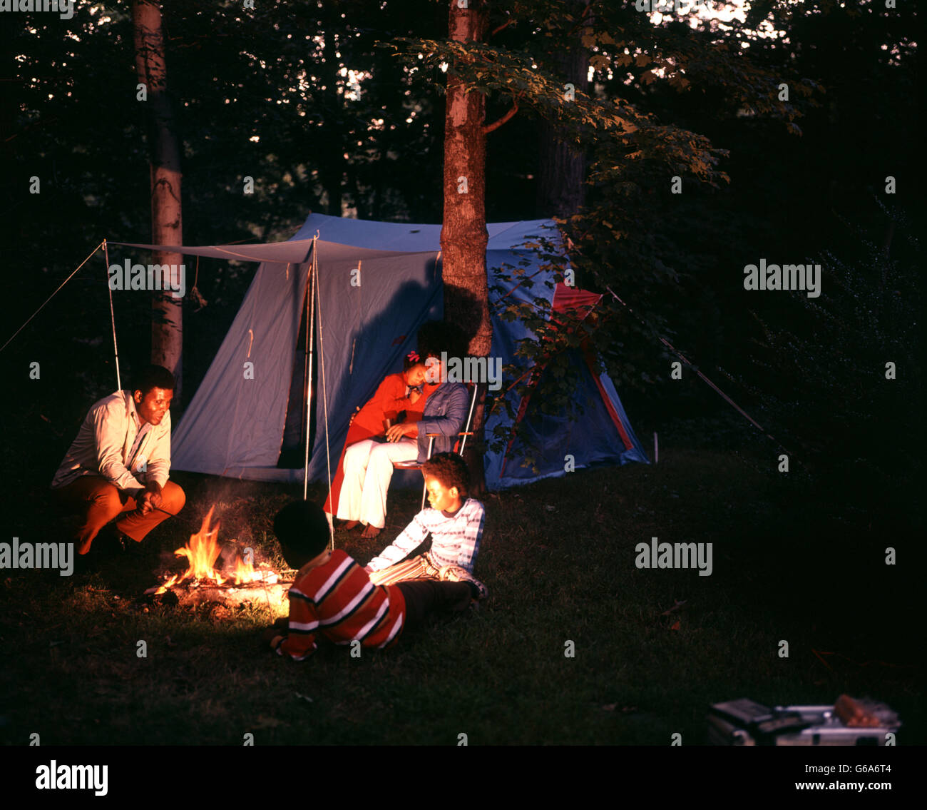 1970ER JAHREN AFROAMERIKANISCHE FAMILIE CAMPING MIT ZELT-NACHT ERSCHOSSEN AM LAGERFEUER SITZEN Stockfoto