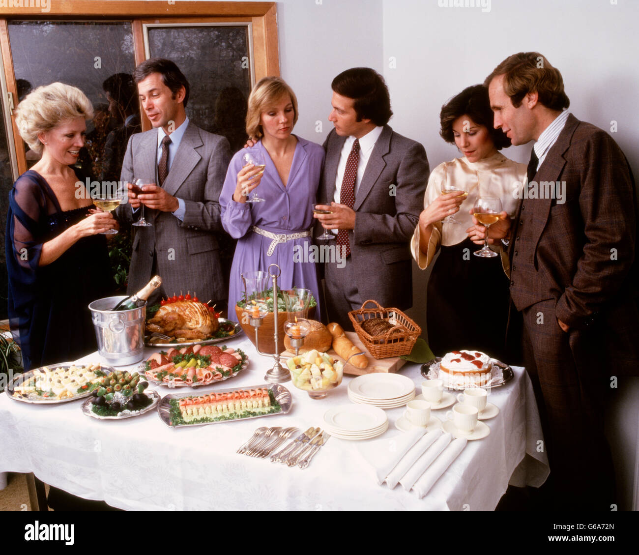 1980ER JAHREN DREI PAARE AM DINNER PARTY CHAT WEIN TRINKEN VOM BUFFET TISCH Stockfoto