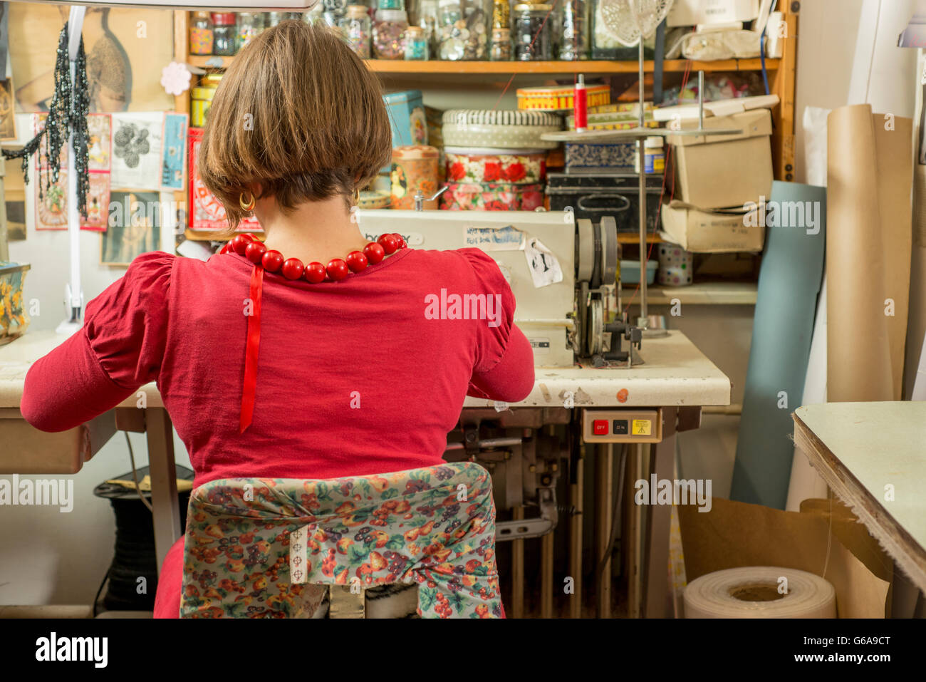 Näherin in rot Sitz, Rücken und arbeiten durch eine Nähmaschine Stockfoto