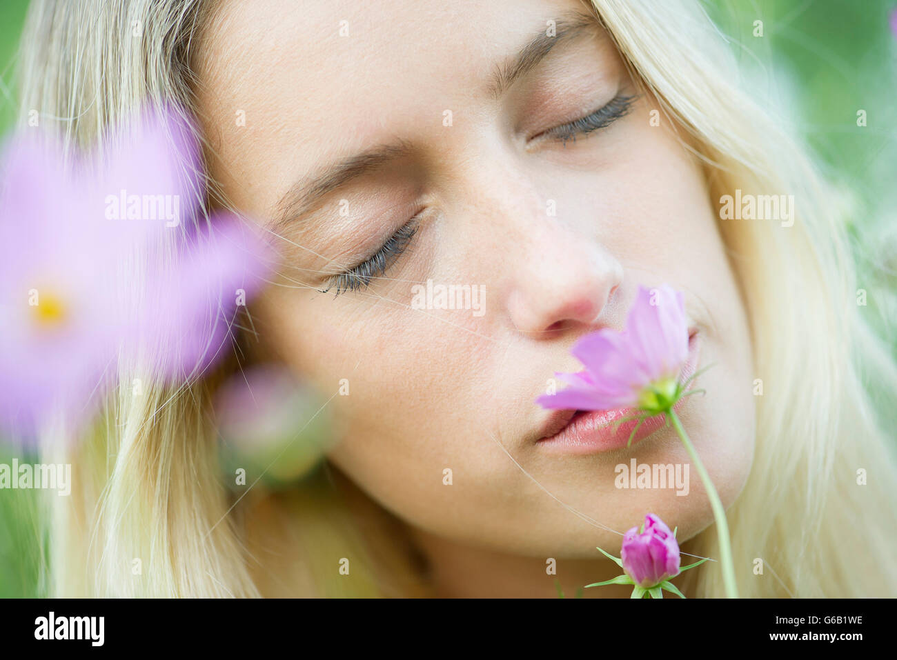 Junge Frau, die duftenden Blüten mit Augen geschlossen, Porträt Stockfoto