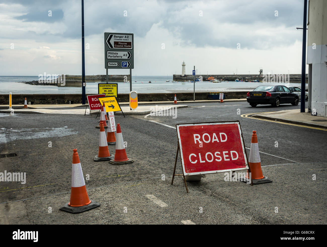 Donaghadee, County Down, UK 24. Juni 2016 Baustellen und Beschilderung Straßenschilder mit Donaghadee Leuchtturm und Hafen im Hintergrund Reparaturen von Fahrbahnoberflächen als Teil der öffentlichen Investitionen Jeffrey Silber/Alamy Live News Stockfoto