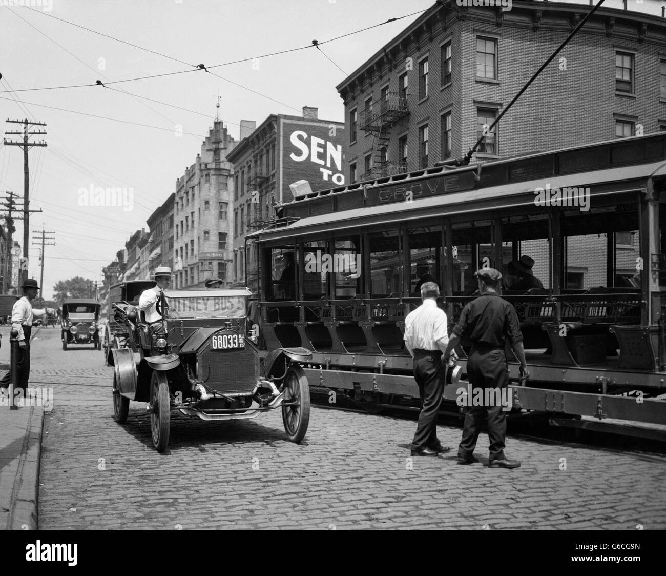 1910ER JAHRE JITNEY BUS UND OFFENE ELEKTRISCHE STRAßENBAHN AUF BRICK STREET IN HOBOKEN, NEW JERSEY USA Stockfoto