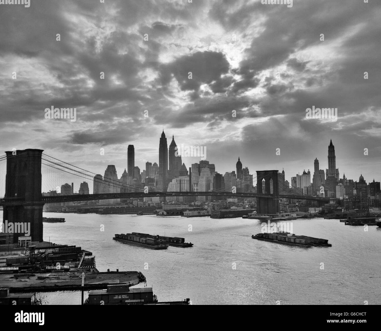 1940S 1950S DRAMATISCHEN SONNENUNTERGANG INNENSTADT LASTKÄHNE SKYLINE VON NEW YORK CITY MIT BROOKLYN BRIDGE IM EAST RIVER NEW YORK NY USA Stockfoto