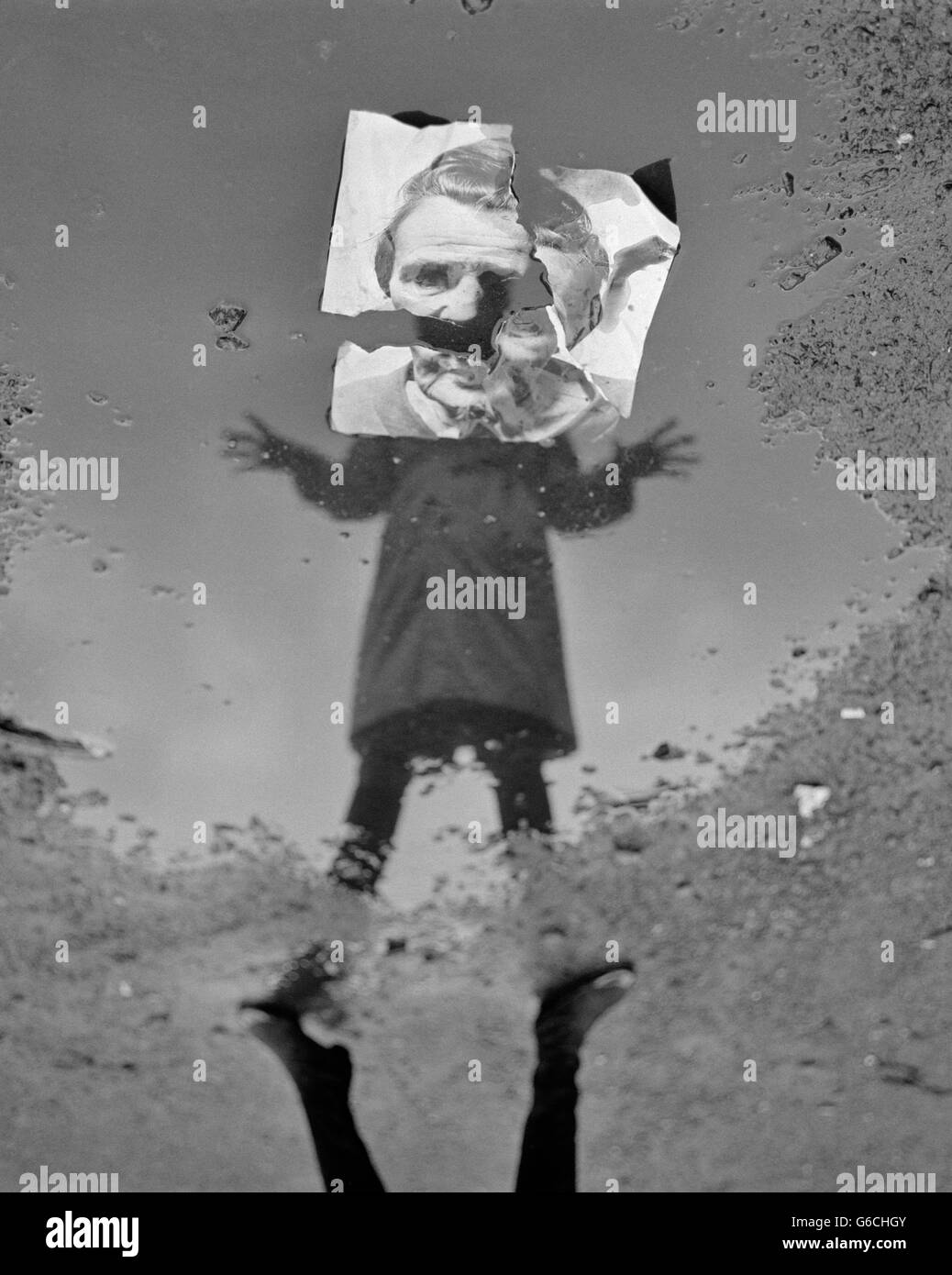 1970ER JAHREN FRAU IM REGENMANTEL, BLICK IN DIE PFÜTZE MIT REFLEXION, ABER GESICHT IST ZERRISSENE FOTO REFLEKTIERENDE SCHMERZEN ANGST PSYCHISCHE KRANKHEIT Stockfoto