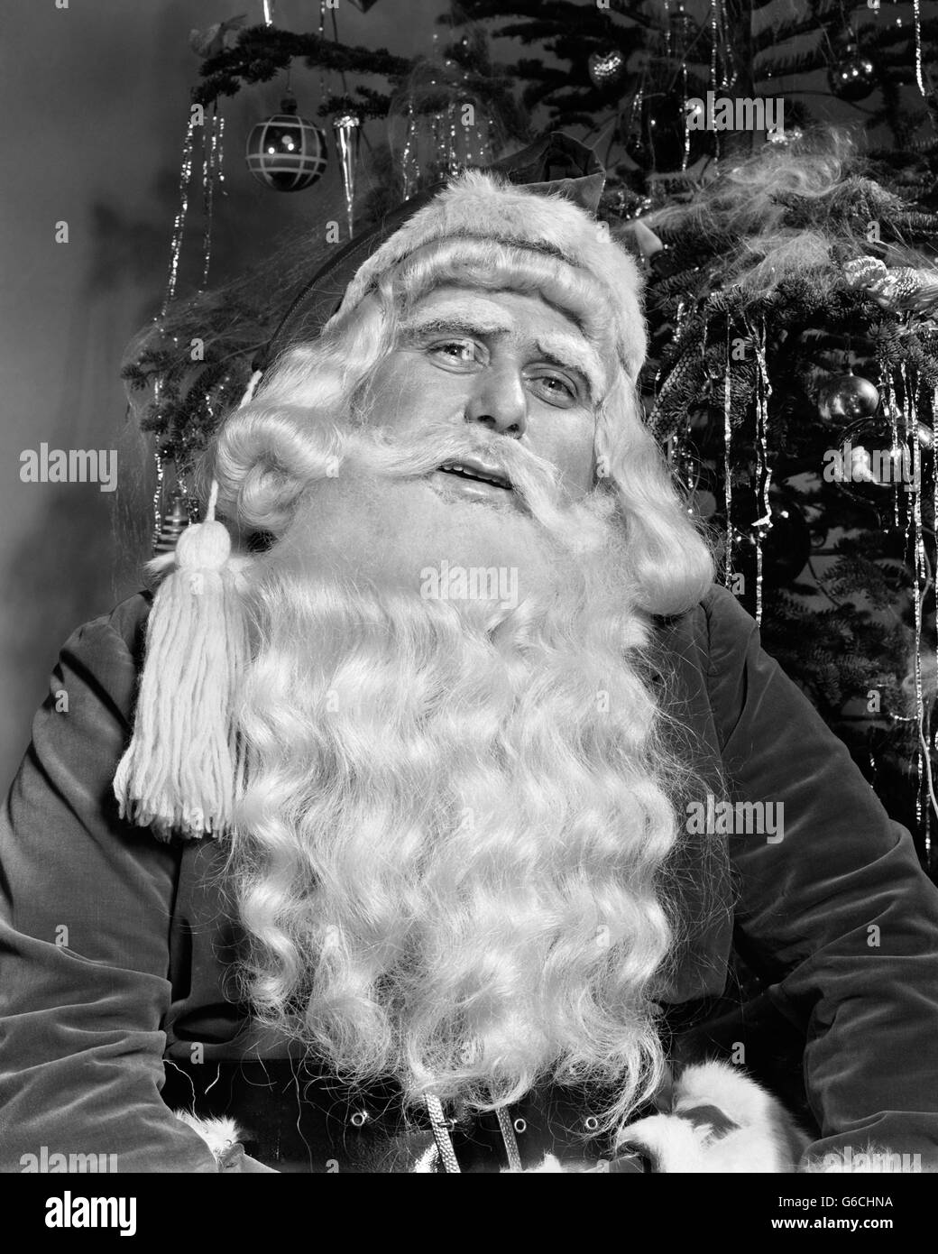 1940ER JAHRE PORTRAIT VON SANTA CLAUS VOR GESCHMÜCKTER WEIHNACHTSBAUM Stockfoto