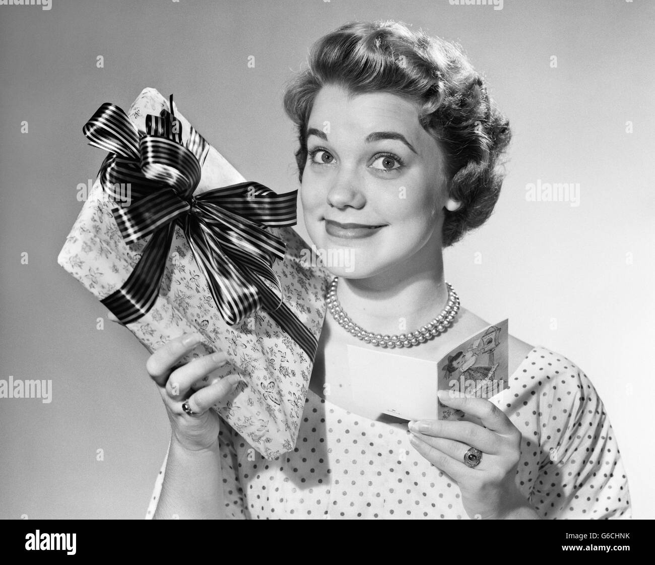 1950ER JAHREN LÄCHELNDE FRAU MIT EINGEWICKELT, GESCHENK- UND GRUßKARTEN-BLICK IN DIE KAMERA Stockfoto