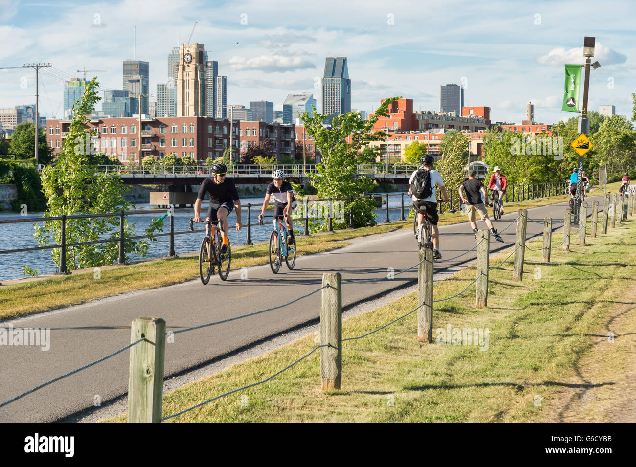 Menschen auf Fahrrädern auf Lachine Canal Radweg in Montreal, mit Skyline im Hintergrund und Atwater market Turm Stockfoto