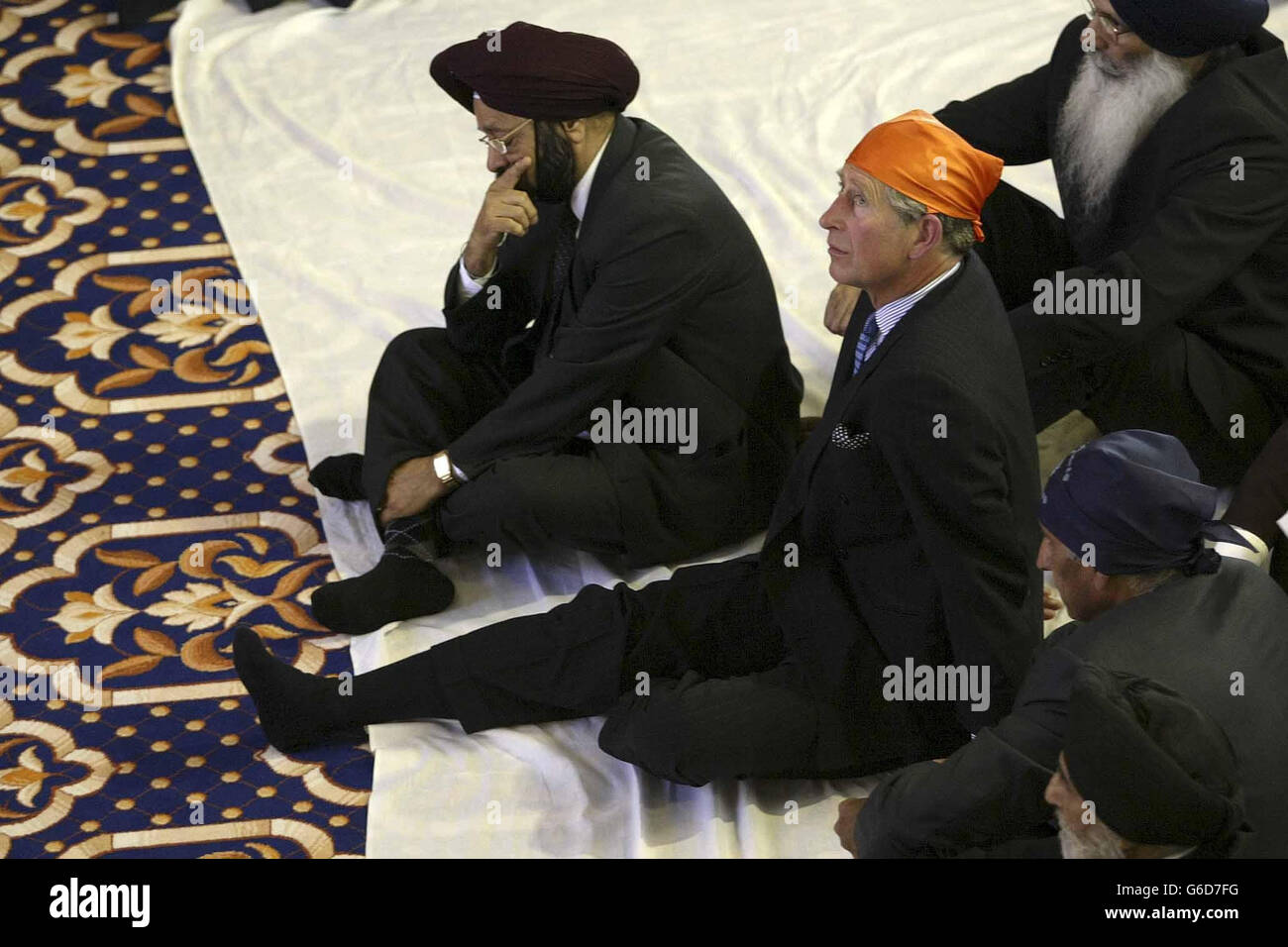 Der Prinz von Wales, trägt ein leuchtend orangefarbenes Ramal Kopftuch im Sri Guru Singh Sabha Gurdwara Sikh Tempel, in Southall. * der Prinz zog auch seine Schuhe aus, um die Sikh-Religion zu respektieren, bevor er zum Gottesdienst geführt wurde, wo er mit gekreuzten Beinen auf einem Kissen saß. Im Gebetsraum wurde für den Prinzen ein Begrüßungslied vorgelesen. Er wurde dann mit einer Siropa am Altar - ein zeremonielles Schwert, ein Gewand der Ehre, ein Tuch für die Königin, und ein Gedenkbuch. Stockfoto
