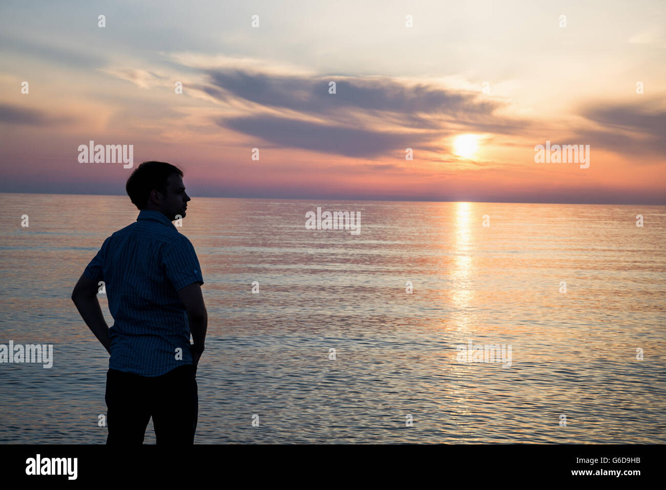 Junger Mann bei Sonnenauf- oder Sonnenuntergang am Strand vor fantastischem Meerblick stehen und über seine Zukunft nachzudenken. Ansicht von hinten Stockfoto