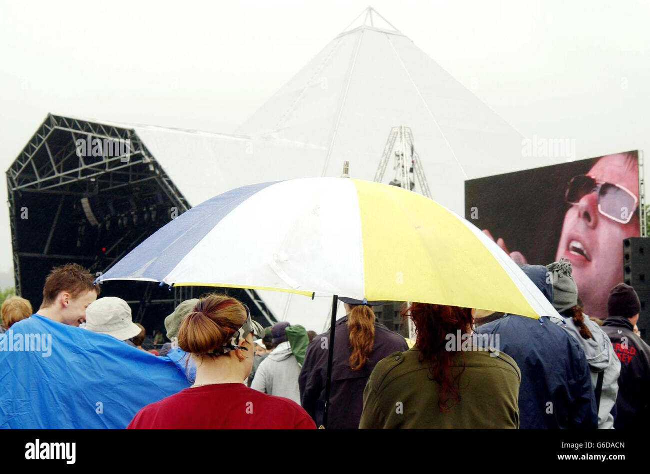 Festivalbesucher trotzen dem Regen während eines Sets von Echo und den Bunnymen auf der Pyramid Stage, beim Glastonbury Festival 2003 in Somerset. Stockfoto