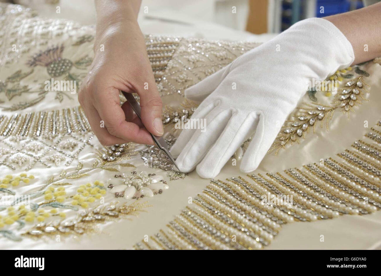 Das Krönungskleid der Königin aus weißem Satin wird für die Sommereröffnung der Buckingham Palace State Rooms von der leitenden Textilkonservatorin Janet Woods bei der Arbeit im Textile Conservation Studio im Hampton Court Palace in SW London vorbereitet. * Wenn das von Norman Hartnell entworfene und mit Stickereien aus Gold- und Silberfäden verzierte Kleid mit Samenperlen und Kristallen geschmückt ist, können die Besucher auch die erste öffentliche Schau des gesamten Krönungsfries von Feliks Topolski sehen. Stockfoto