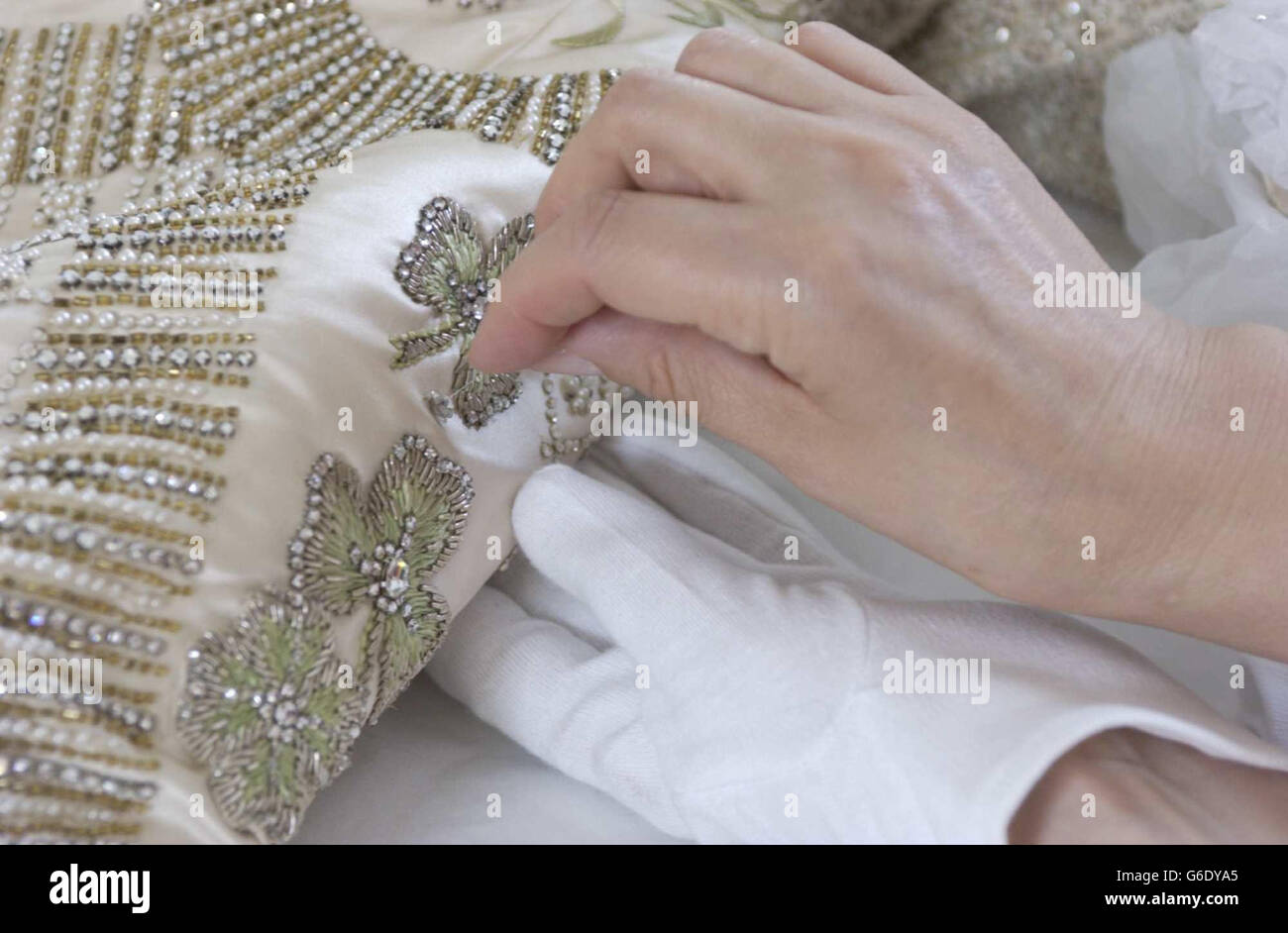 Das Krönungskleid der Königin aus weißem Satin wird für die Sommereröffnung der Buckingham Palace State Rooms von der leitenden Textilkonservatorin Janet Woods bei der Arbeit im Textile Conservation Studio im Hampton Court Palace in SW London vorbereitet. * Wenn das von Norman Hartnell entworfene und mit Stickereien aus Gold- und Silberfäden verzierte Kleid mit Samenperlen und Kristallen geschmückt ist, können die Besucher auch die erste öffentliche Schau des gesamten Krönungsfries von Feliks Topolski sehen. Stockfoto