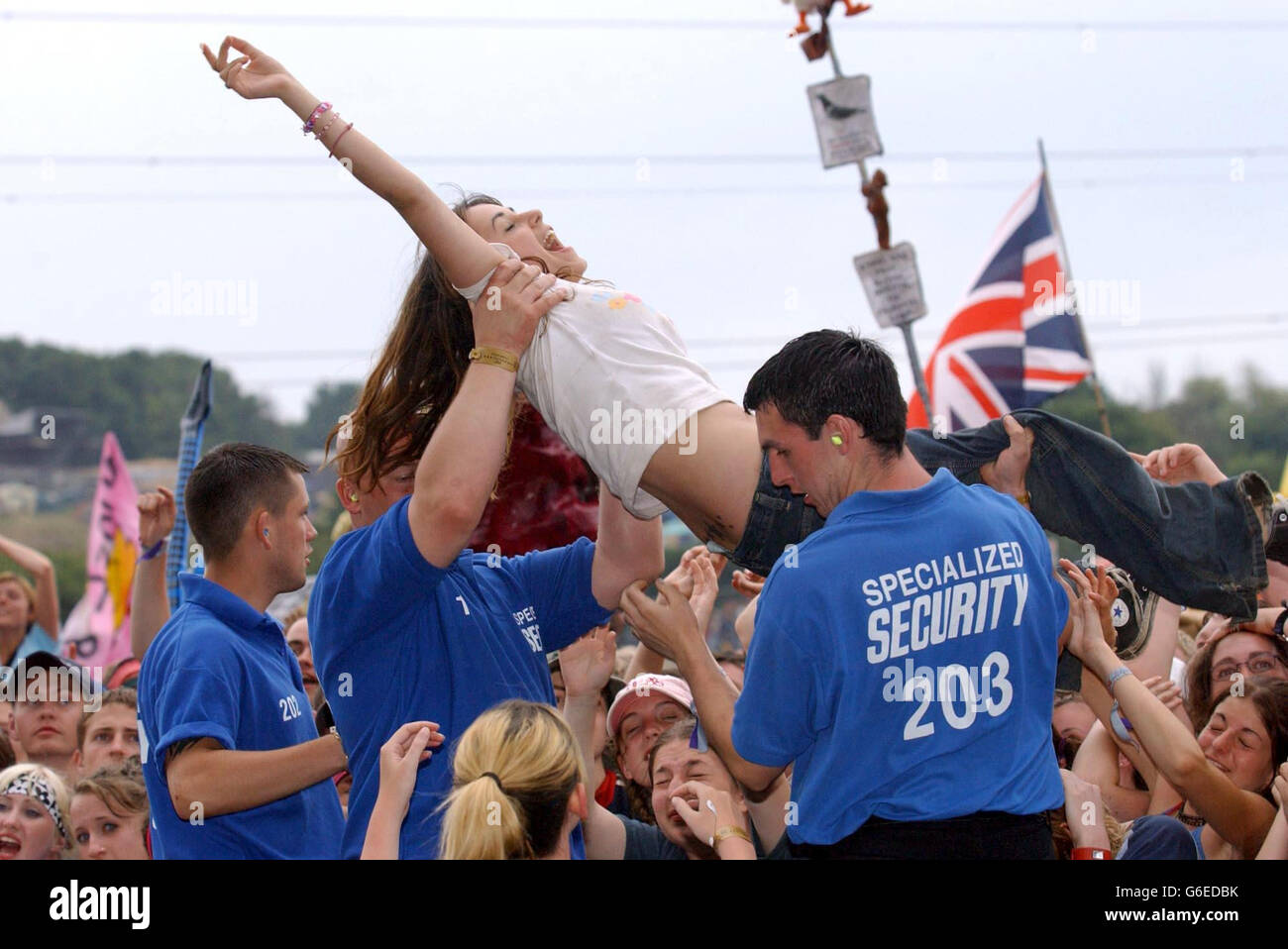 Ein Mädchen wird vom Sicherheitsdienst aus der Menge gezogen, während Feeder beim Glastonbury Festival 2003 auftreten sieht. Stockfoto