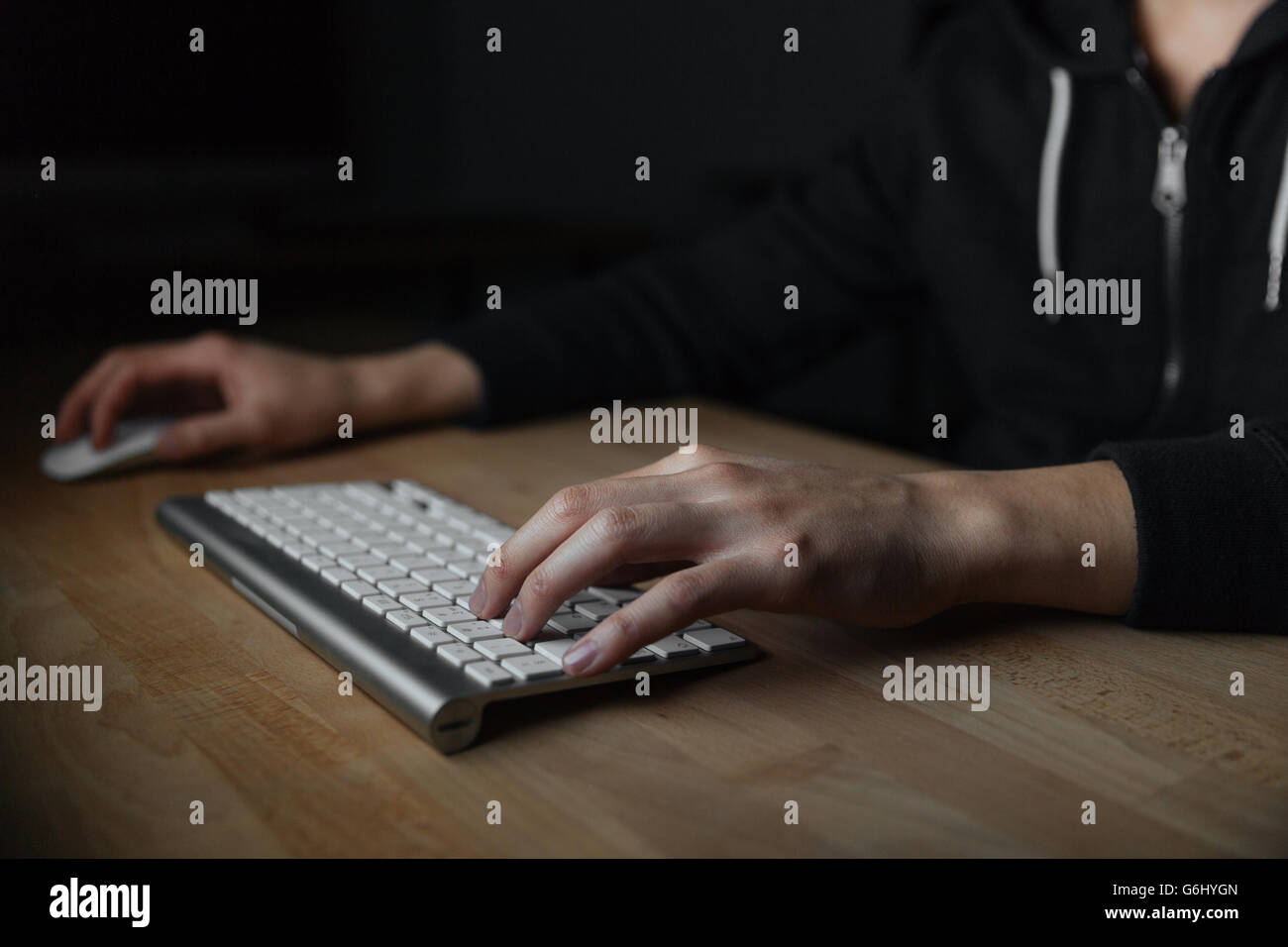 Händen der junge Mann am Tisch sitzen und schreiben auf der Tastatur in dunklen Raum Stockfoto