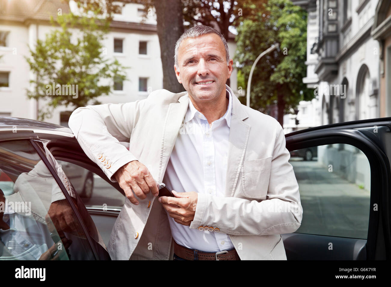 Porträt von lächelnder Mann lehnt sich an offene Autotür mit Autoschlüssel Stockfoto