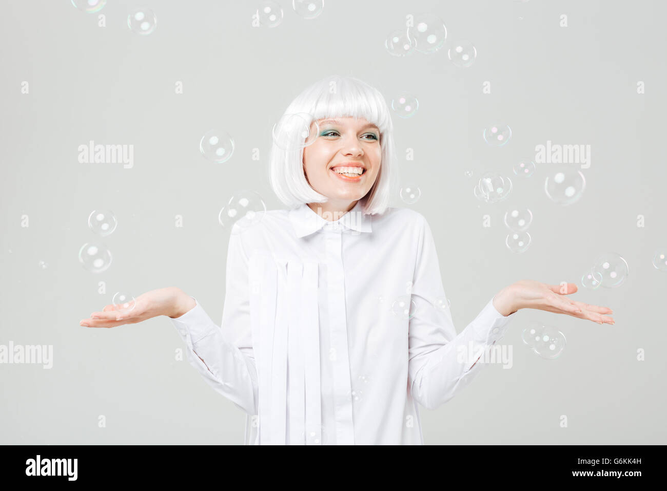 Gerne schöne junge Frau genießen Seifenblasen und hält Exemplar auf Handflächen über weißem Hintergrund Stockfoto