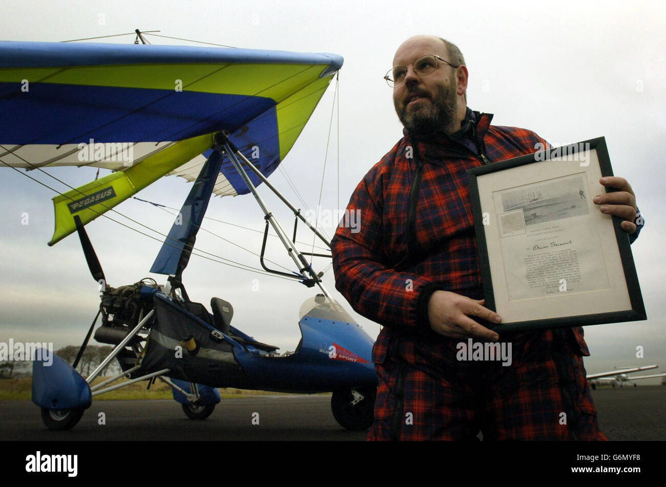 Colin Mackinnon mit seinem Fragment aus Flügelgewebe aus dem weltweit ersten angetriebenen Flugzeug, das die Gebrüder Wright am 100. Jahrestag des Fluges am Flughafen Cumbernauld geflogen haben. In ihrem revolutionären motorisierten "Flyer" eroberten die Brüder als erste am 17. Dezember 1903 die Luft und flogen über eine abgelegene Sandinsel an der Atlantikküste von North Carolina, USA. Stockfoto