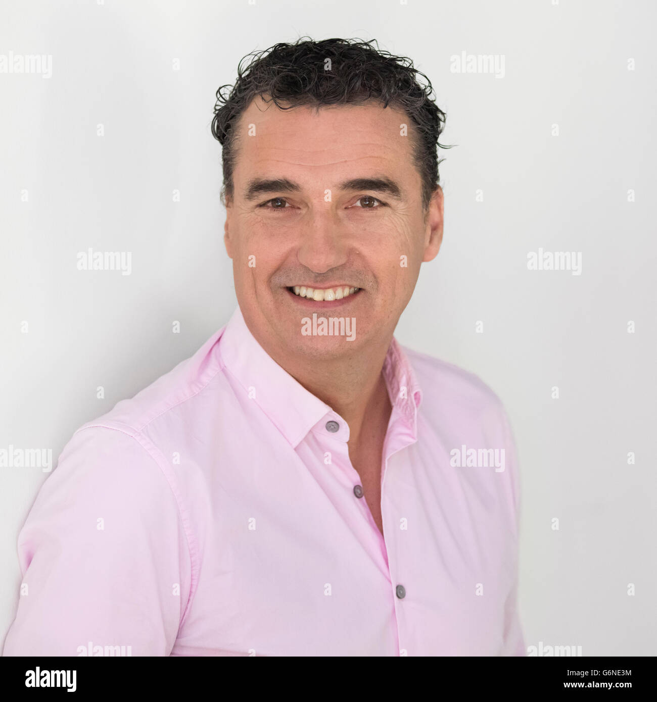 Glücklich der 50er Jahre kaukasischen Geschäftsmann in rosa Hemd Blick auf Kamera, weißer Hintergrund Stockfoto