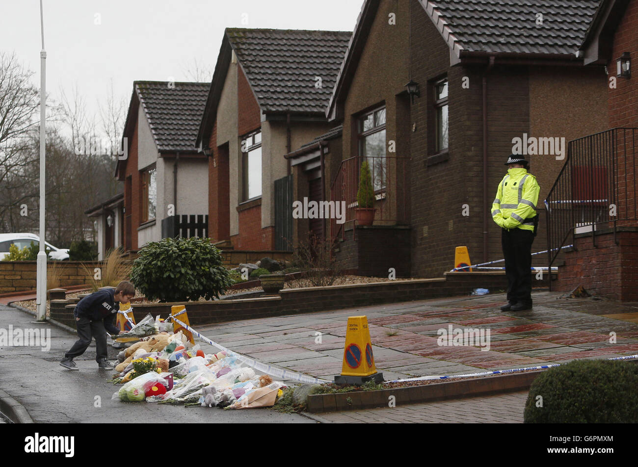 Ein kleiner Junge mit floralen Ehrungen auf der Dunvegan Avenue in Kirkcaldy, Schottland, nachdem die Polizei den Leichnam eines Kindes entdeckt hatte, das nach dem vermissten dreijährigen Mikaeel Kular suchte. Stockfoto