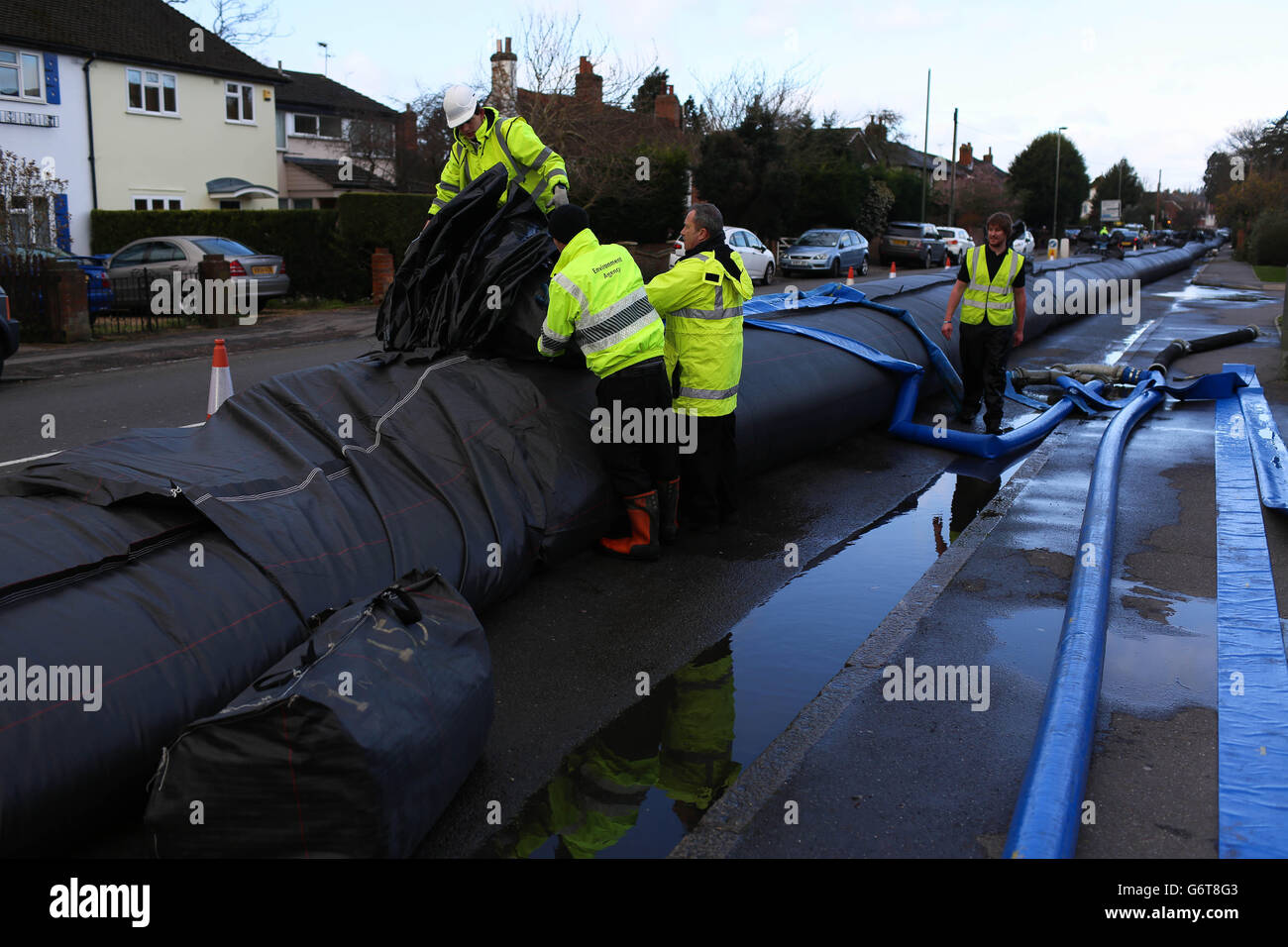 In Chertsey, Surrey, installieren Arbeiter einen Wasserdamm, um Häuser vor dem erwarteten Hochwasser zu schützen, da zwei Menschen gestorben sind und Zehntausende Häuser ohne Strom sind, da Großbritanniens Unwetter weiterhin Überschwemmungsmiserei in Teilen des Landes verursacht. Stockfoto