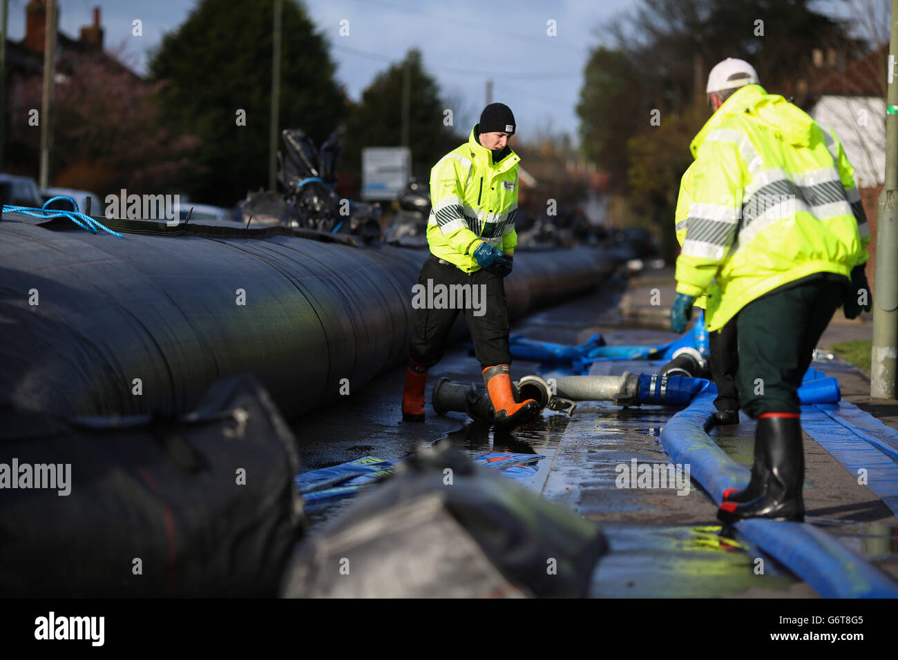 In Chertsey, Surrey, installieren Arbeiter einen Wasserdamm, um Häuser vor dem erwarteten Hochwasser zu schützen, da zwei Menschen gestorben sind und Zehntausende Häuser ohne Strom sind, da Großbritanniens Unwetter weiterhin Überschwemmungsmiserei in Teilen des Landes verursacht. Stockfoto