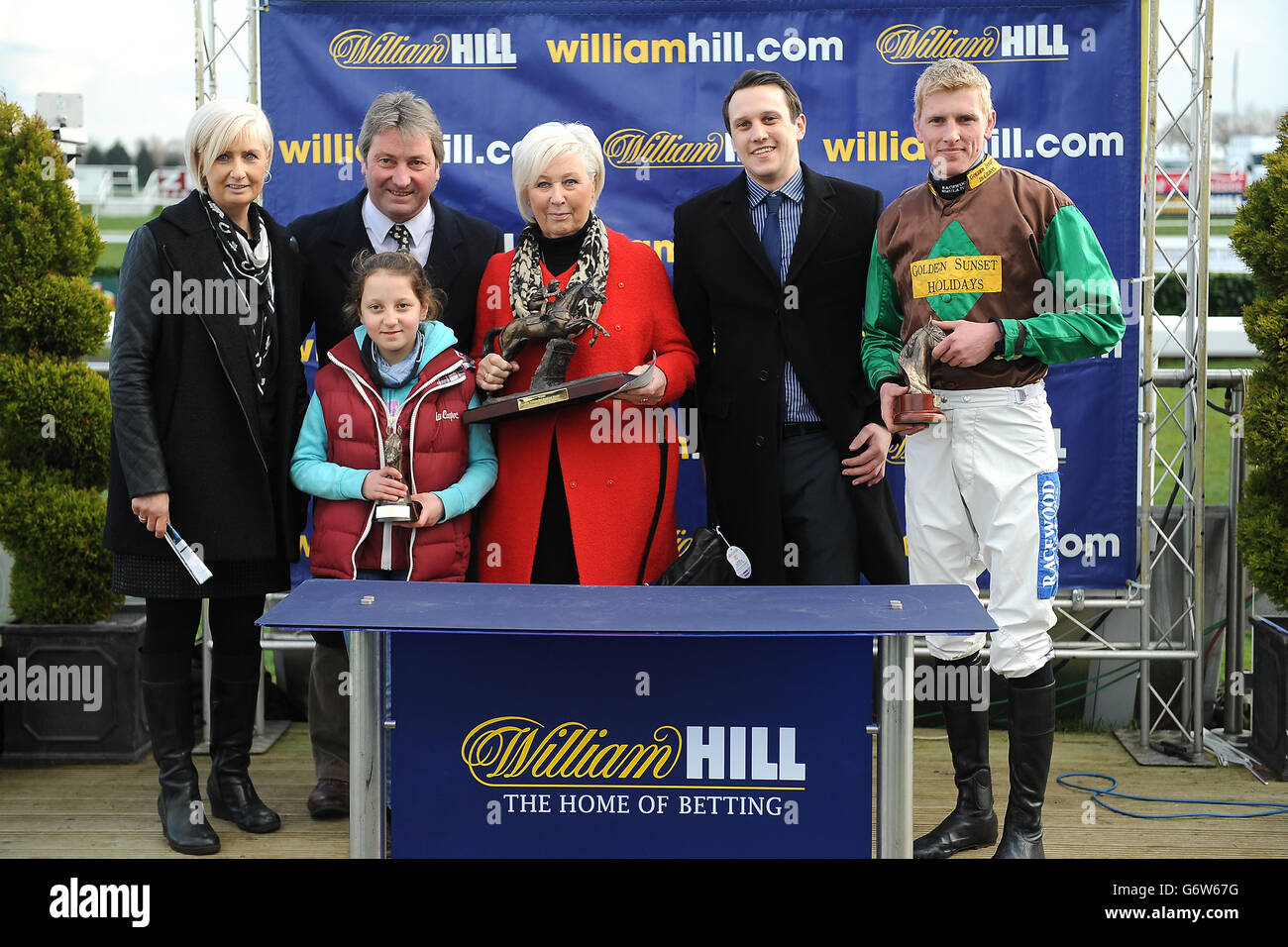 Doeslessthanme-Trainer Richard Ford (hinten, zweiter rechts) und Jockey Harry Challoner (rechts) mit der Trophäe nach dem Sieg im William Hill - im App Store Handicap Chase Stockfoto