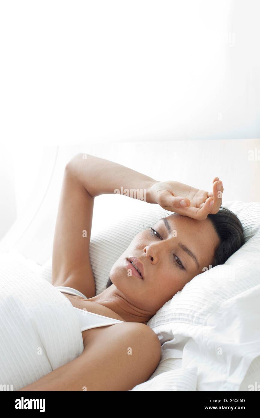 -MODELL VERÖFFENTLICHT. Junge Frau im Bett mit der Hand auf der Stirn. Stockfoto