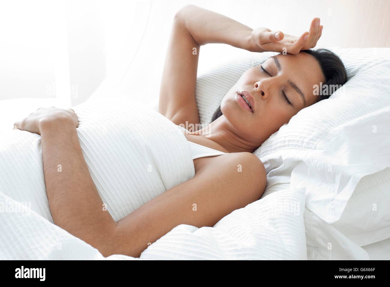 -MODELL VERÖFFENTLICHT. Junge Frau im Bett mit der Hand auf der Stirn. Stockfoto