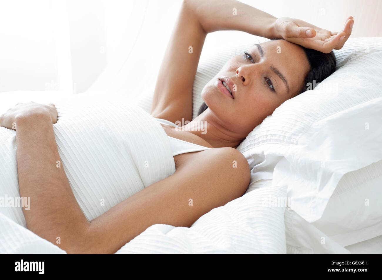 -MODELL VERÖFFENTLICHT. Junge Frau im Bett mit der Hand auf der Stirn. Stockfoto