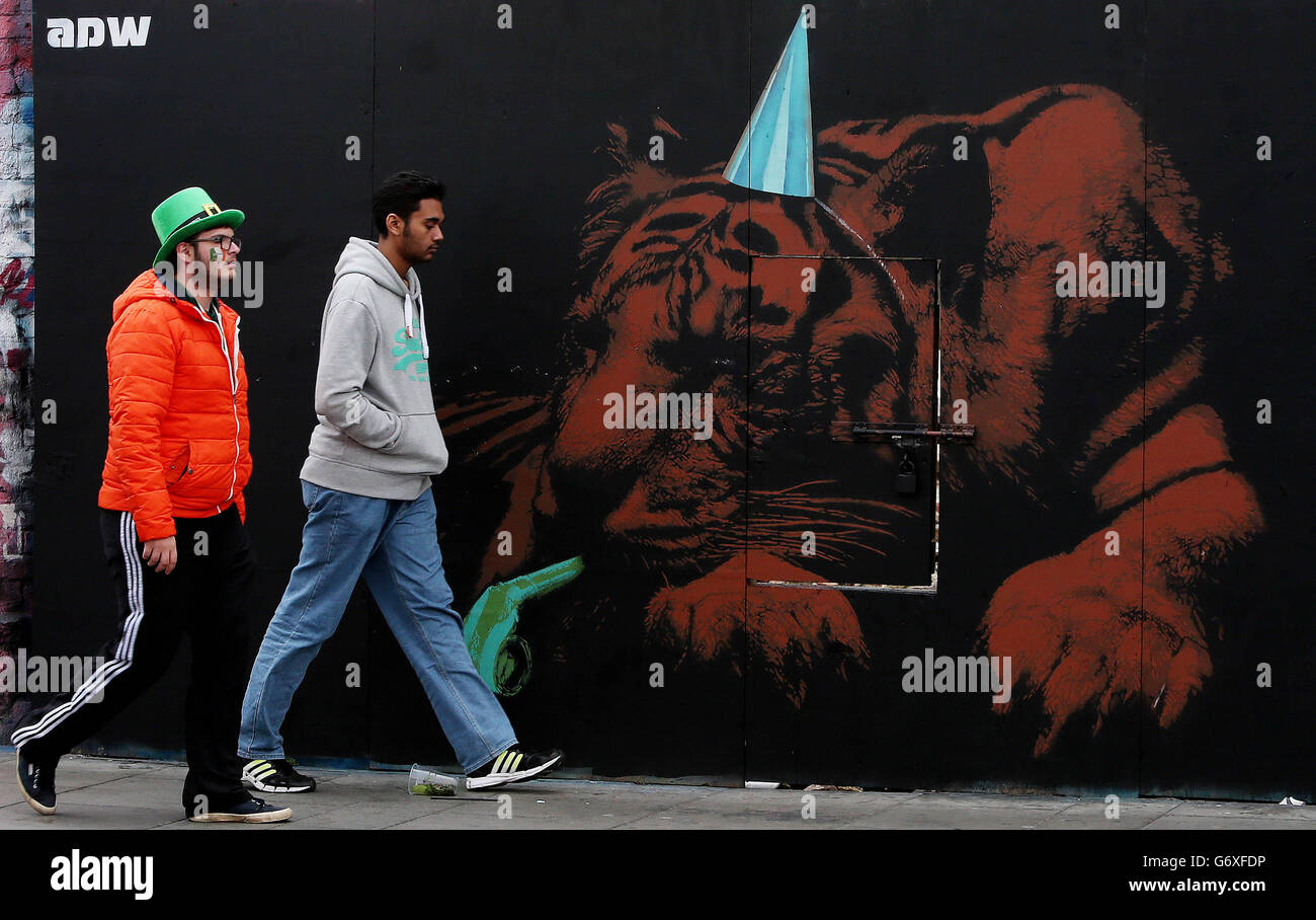 Die Leute kommen an einem neuen Graffiti-Werk vorbei, das den keltischen Tiger zeigt, der sich von zu viel Party ausruhen lässt, erstellt von der Straßenkünstlerin ADW, als sie von der Dublin St. Patrick's Day Parade nach Hause gehen. Stockfoto